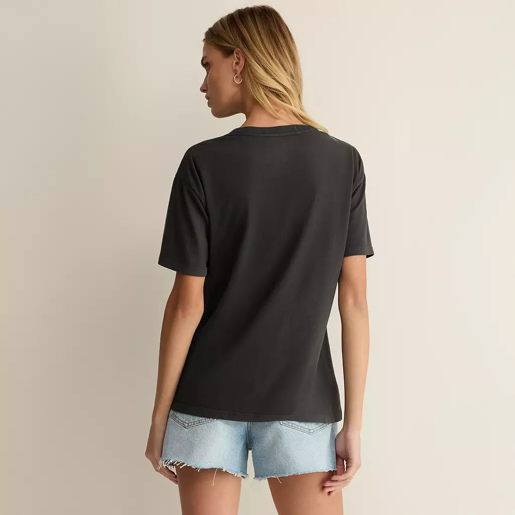 A woman shown from the back wearing an oversized black short-sleeve t-shirt and light-wash denim shorts against a plain beige studio background.