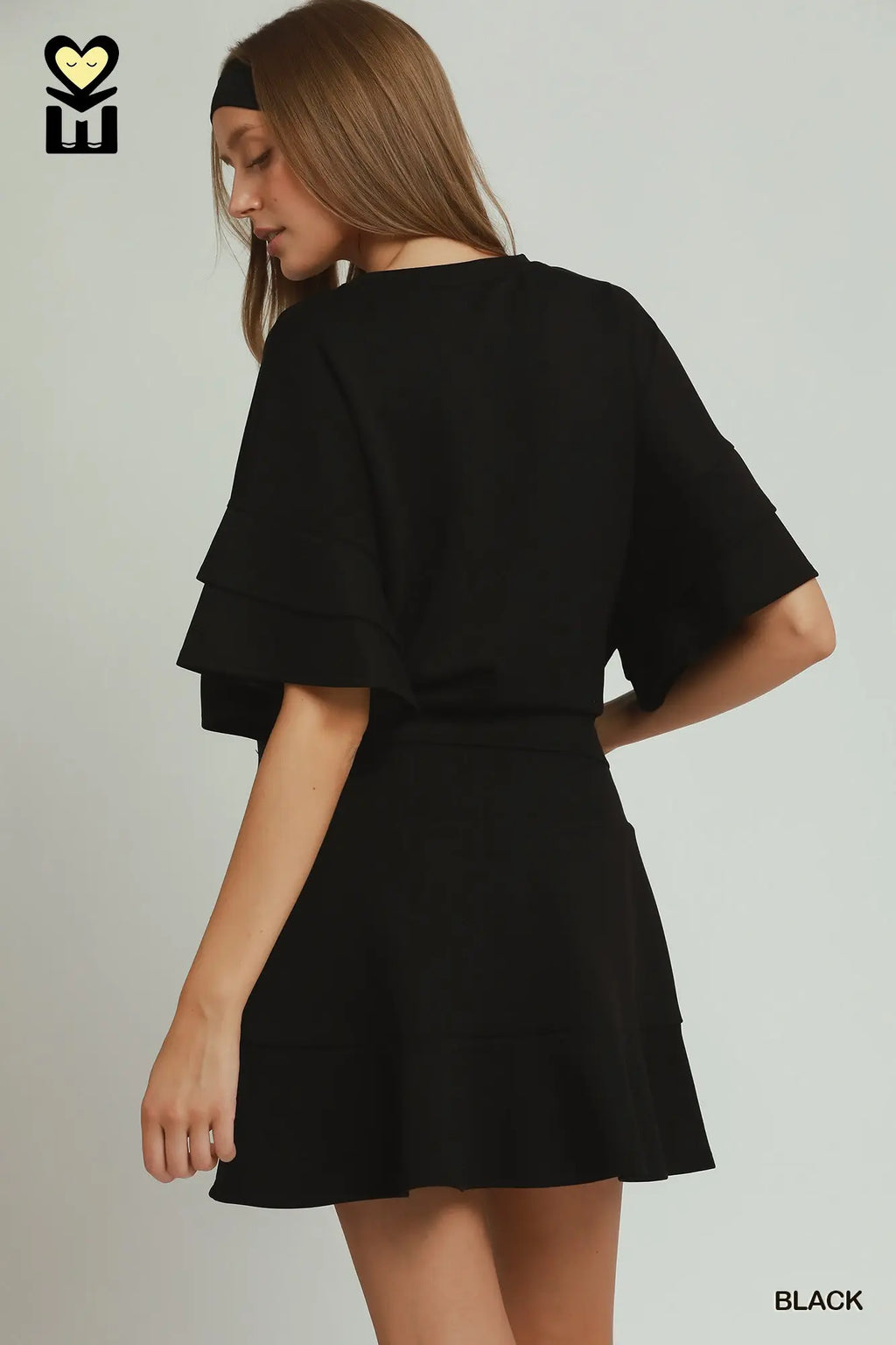 Woman wearing a black dress with ruffled sleeves on a plain background