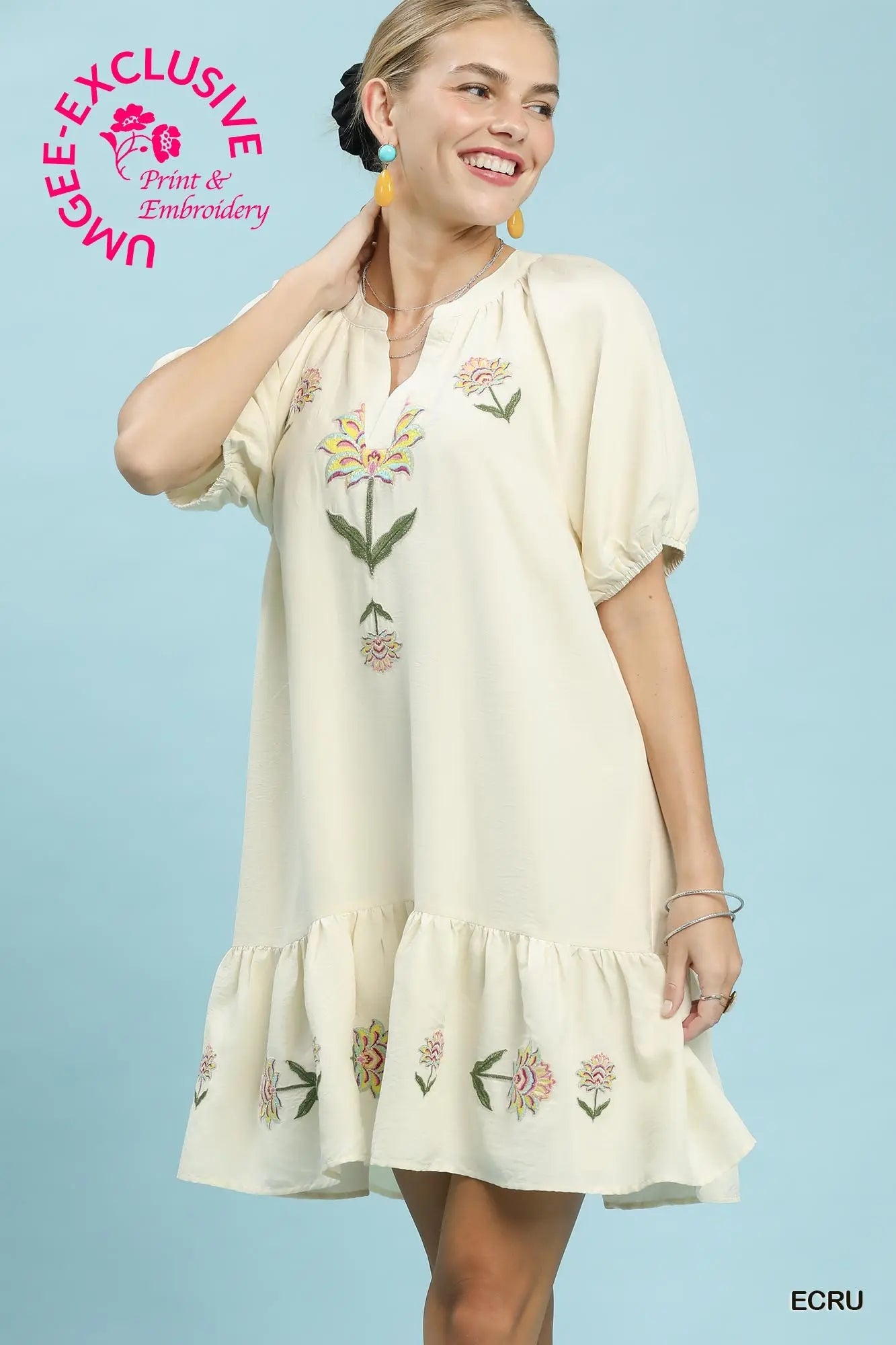 Woman wearing a cream-colored dress with floral embroidery against a light blue background