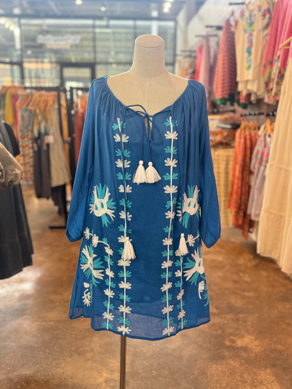 Blue dress with white floral embroidery on a mannequin in a store setting