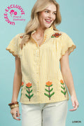 Woman wearing a yellow blouse with floral embroidery on a light blue background