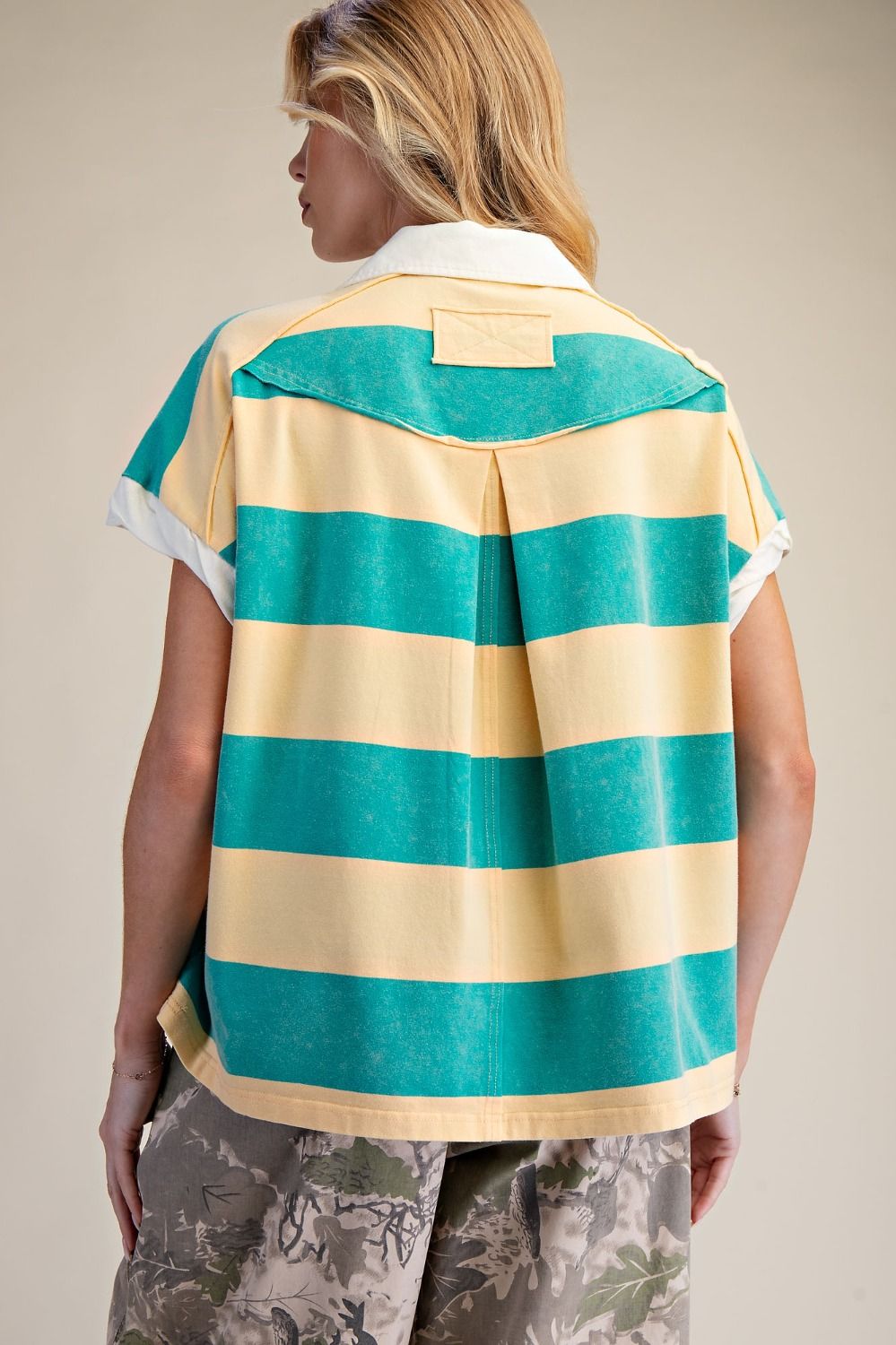 Person wearing a yellow and green striped shirt with a beige collar on a neutral background