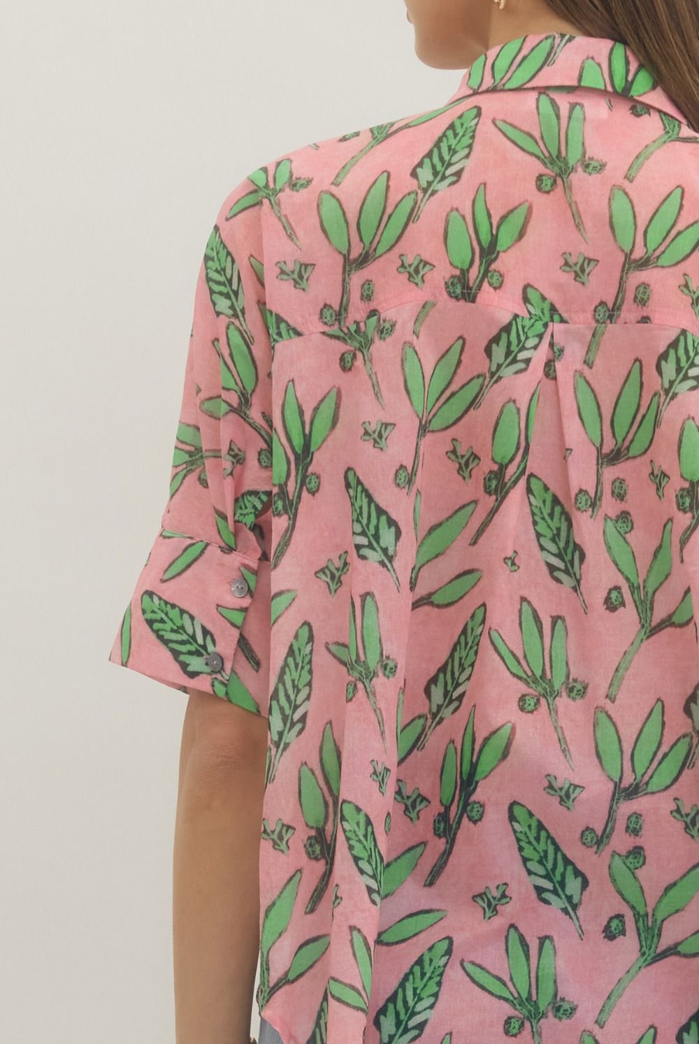 Pink shirt with green leaf pattern worn by a person on a plain background