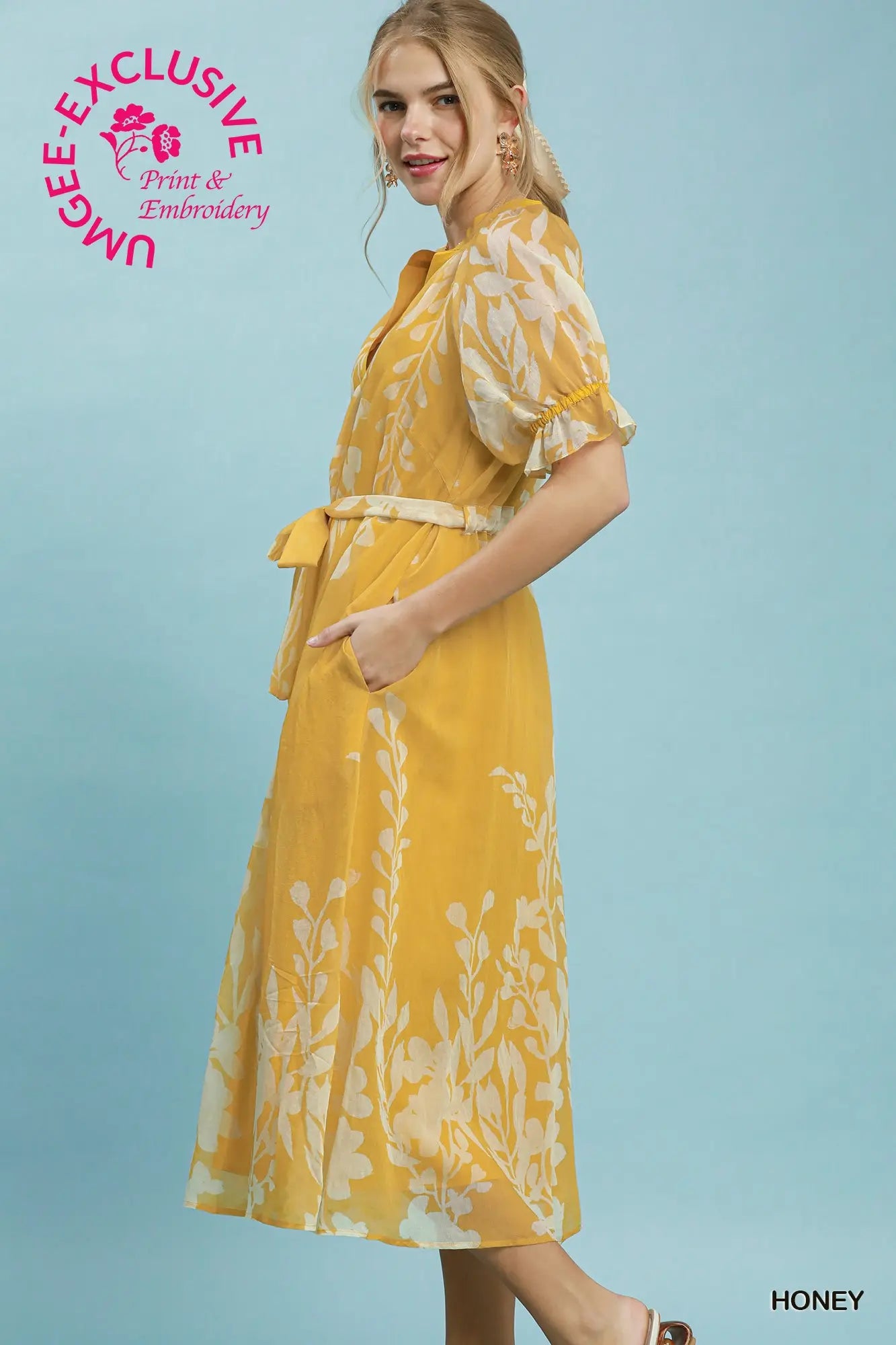 Woman wearing a yellow dress with floral pattern on a blue background, featuring Umgee Exclusive branding.