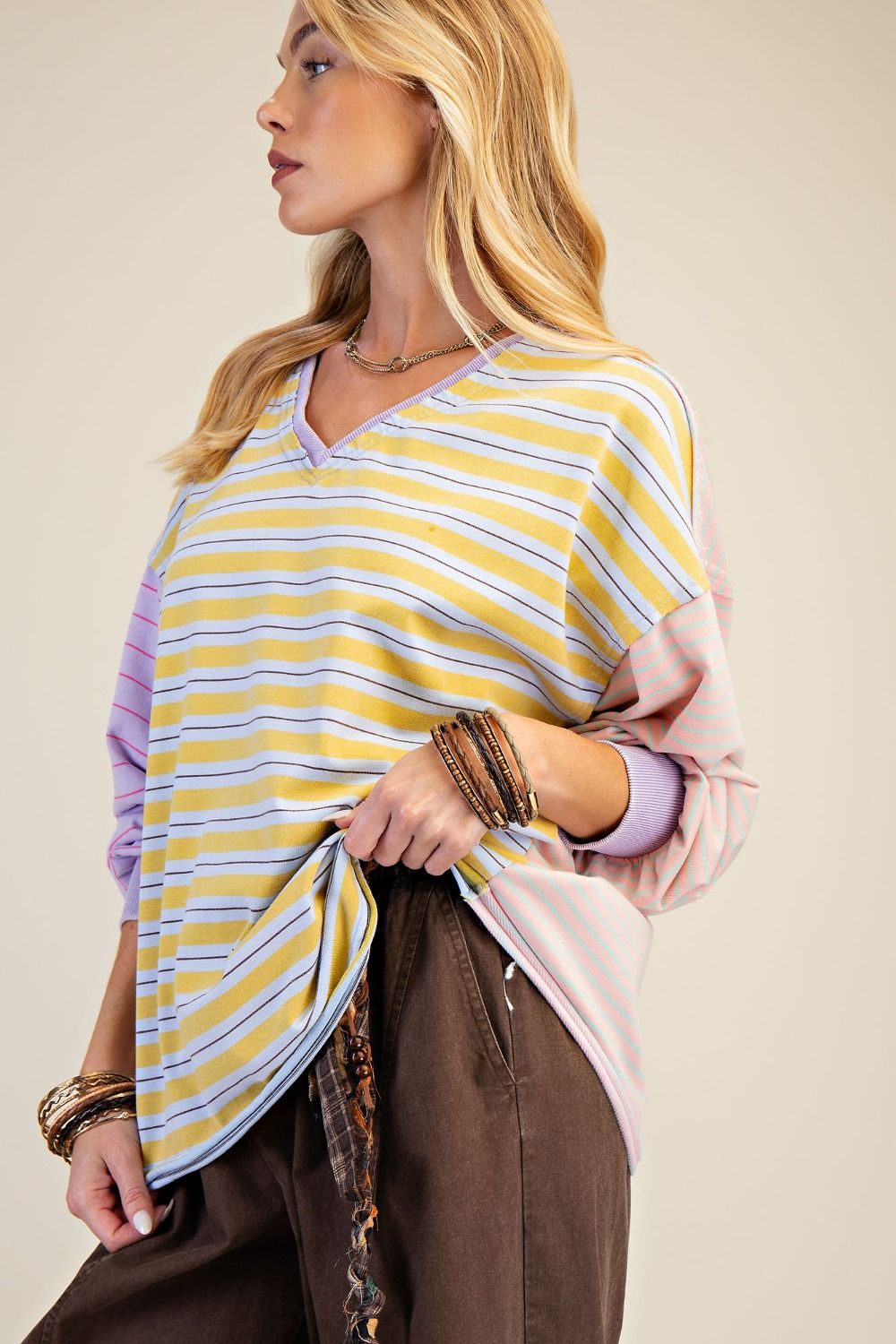 Woman wearing a yellow and purple striped shawl over a pink top against a beige background