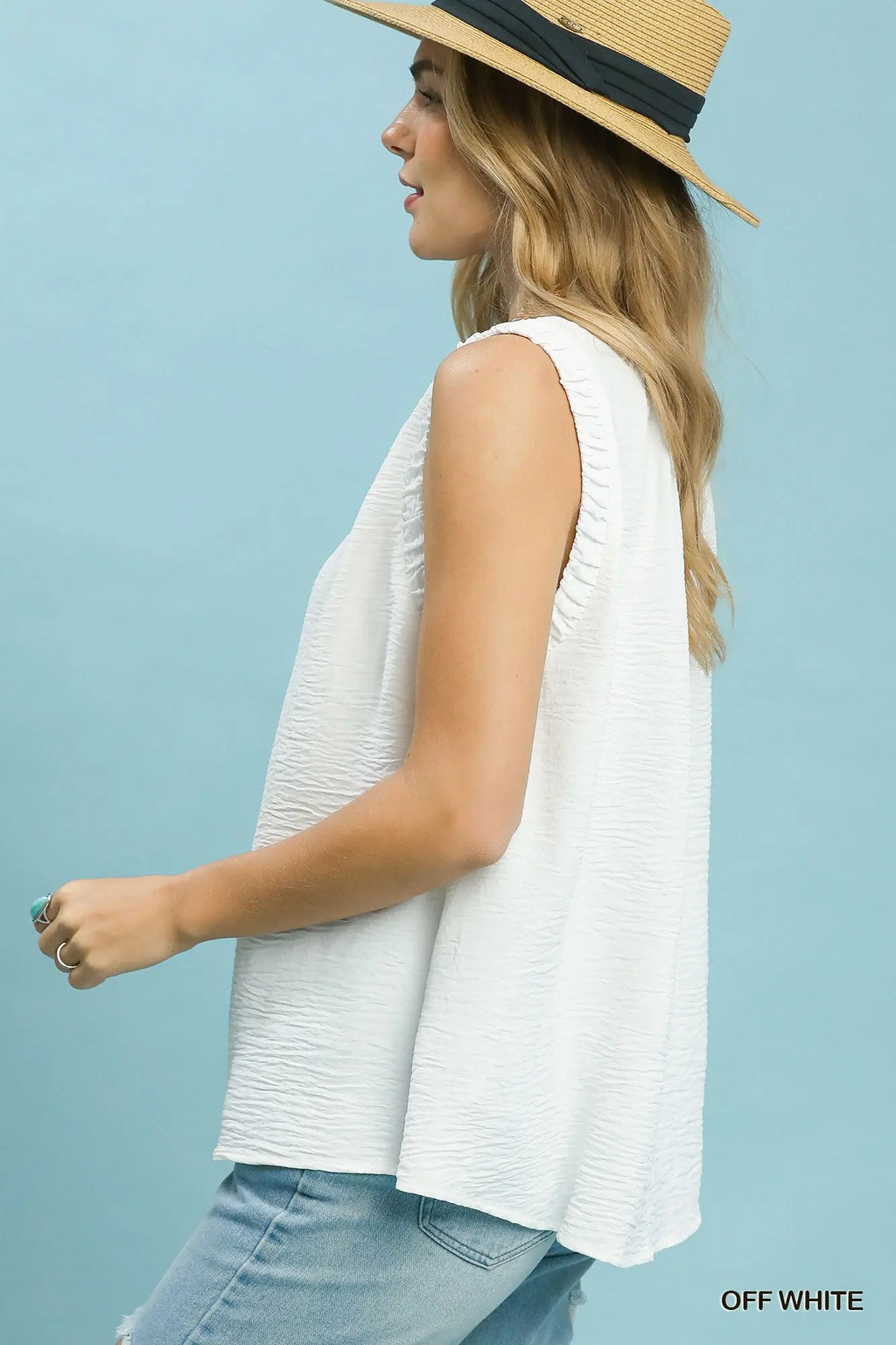 Woman wearing a white sleeveless top and straw hat against a light blue background