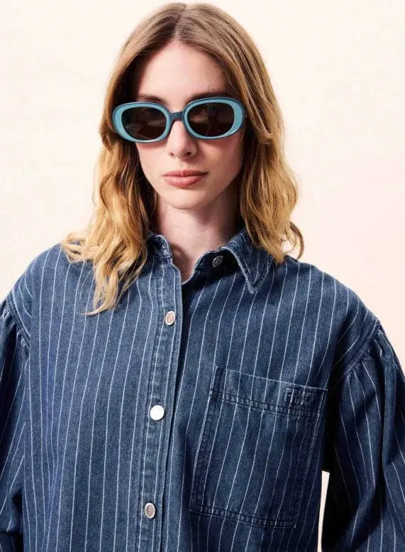 Person wearing a blue striped shirt and sunglasses against a light background