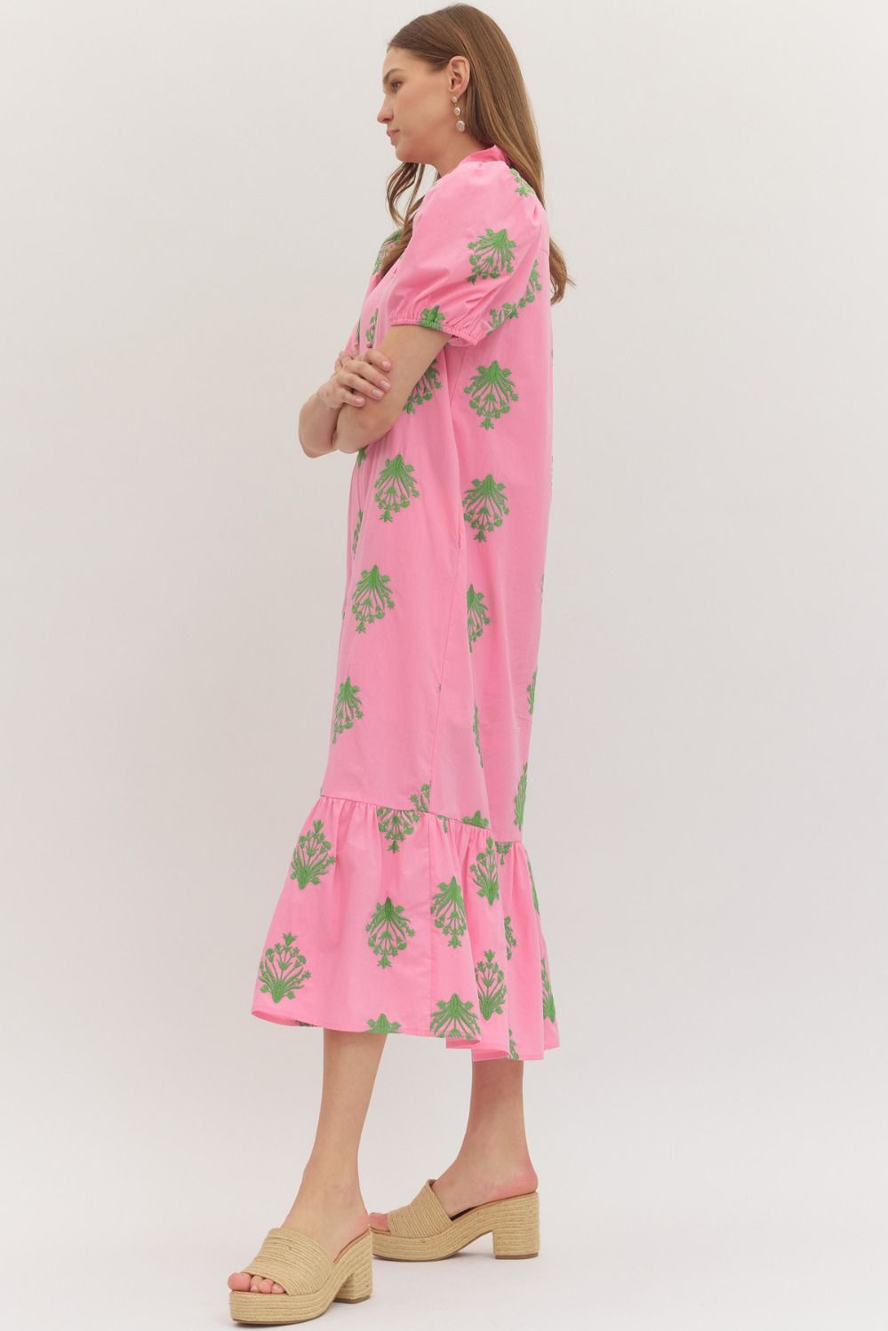 Woman wearing a pink dress with green floral patterns on a white background