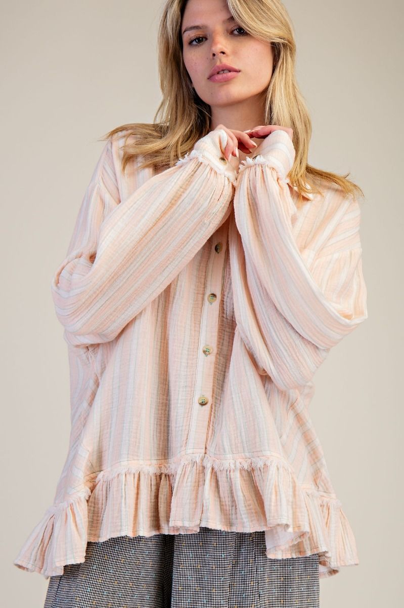 Woman wearing a light pink and white striped blouse with ruffled details on a plain background
