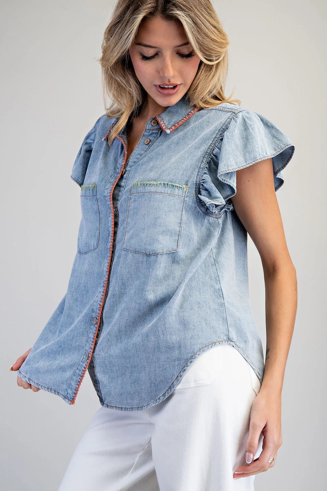 Woman wearing a light blue denim shirt with ruffled sleeves on a plain background