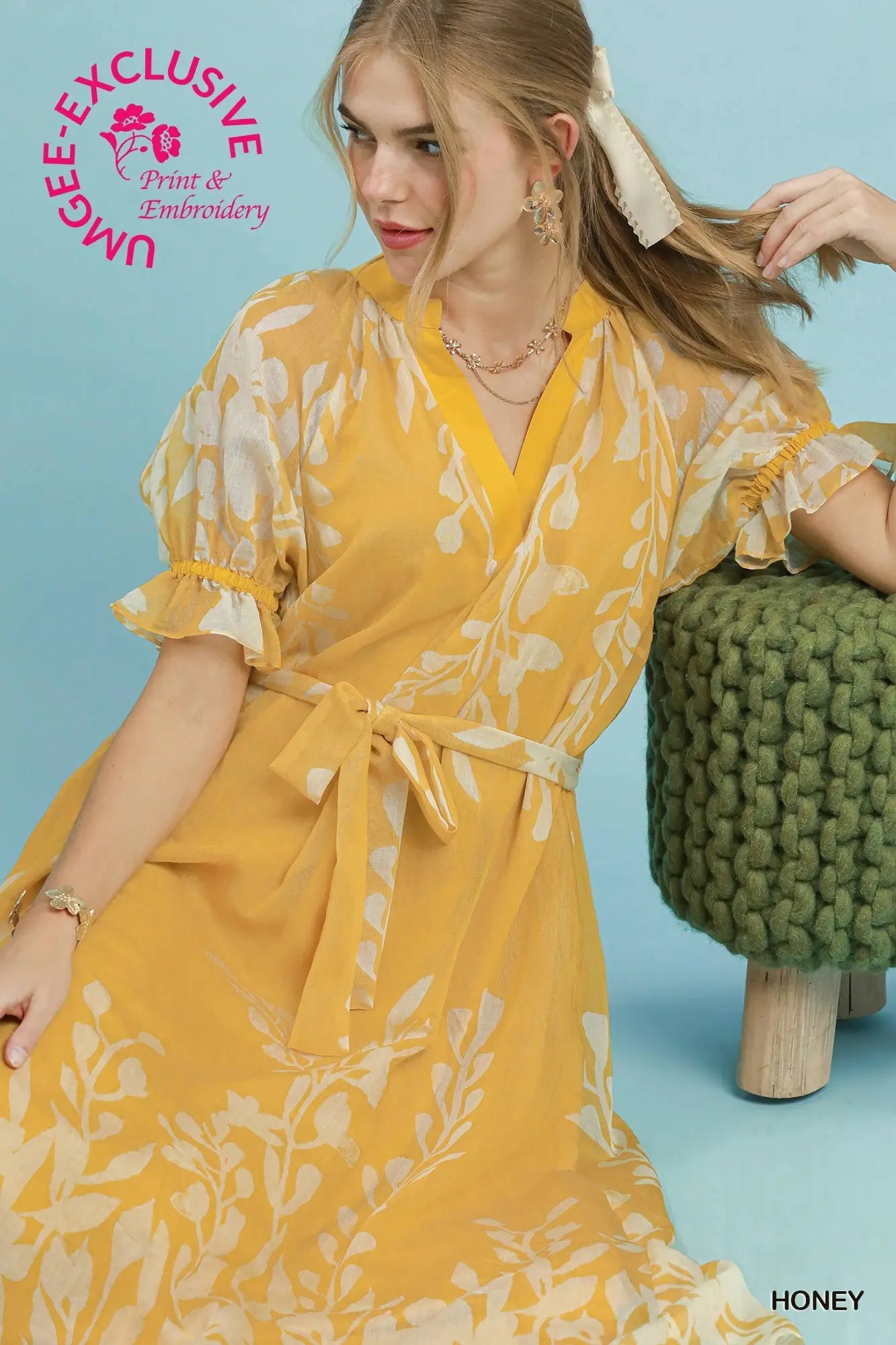 Woman wearing a yellow floral dress against a blue background with 'UMEE Exclusive' branding.