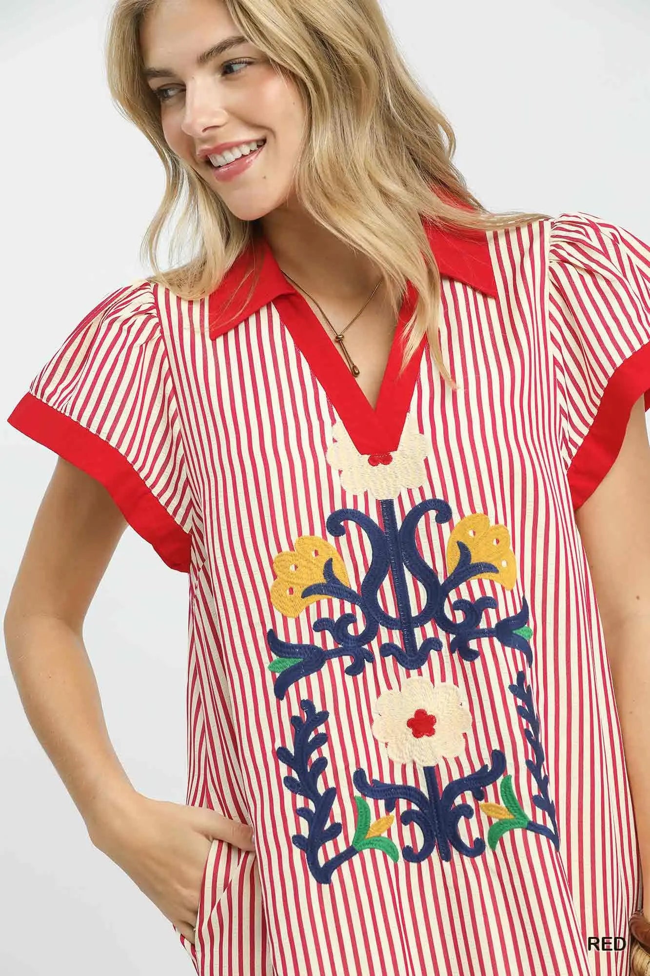 Woman wearing a red and white striped dress with floral embroidery on a plain background