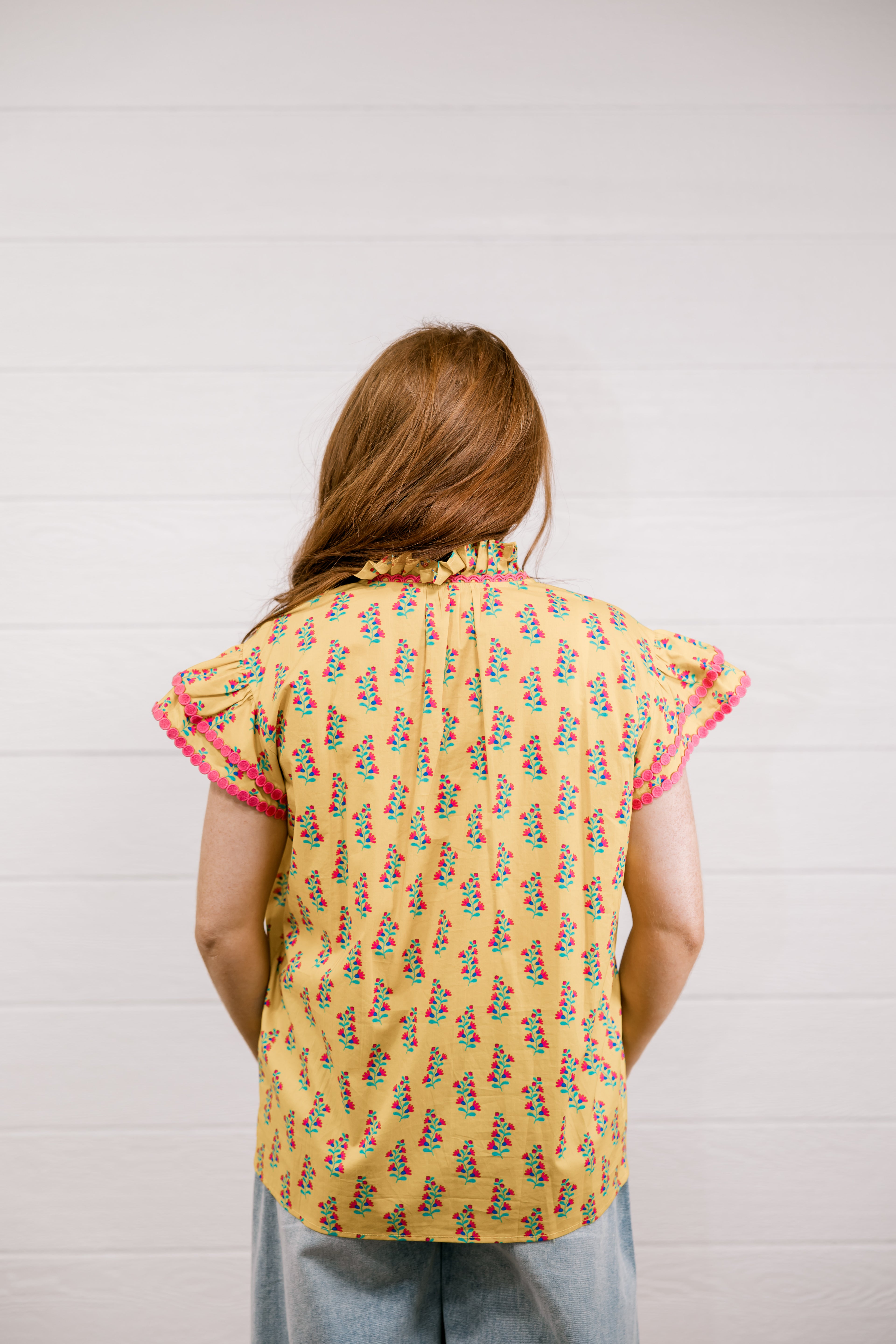 Person wearing a yellow floral sleeveless top with pink trim against a white background