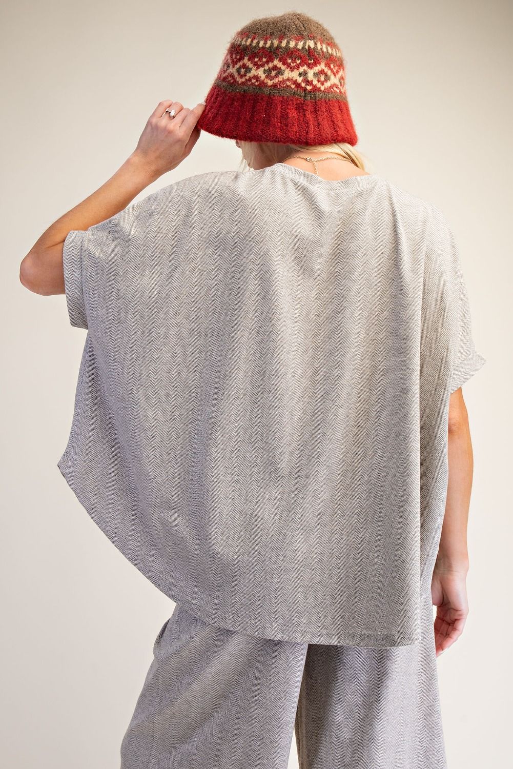 Person wearing a red patterned hat and gray outfit on a plain background