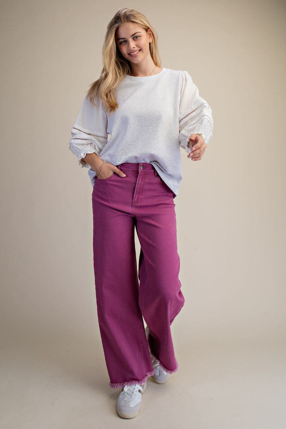 Woman wearing a white sweater and pink pants on a beige background