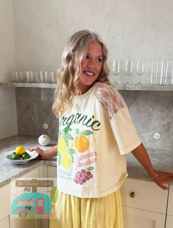 Woman in a kitchen wearing a 'Summer Produce' t-shirt with fruits and vegetables.