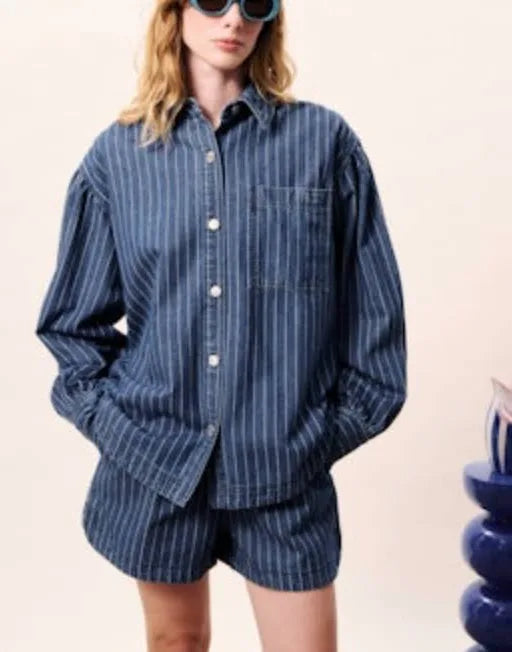 Person wearing a blue striped shirt and shorts with a beige background