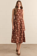 Woman wearing a brown floral dress against a white brick wall.