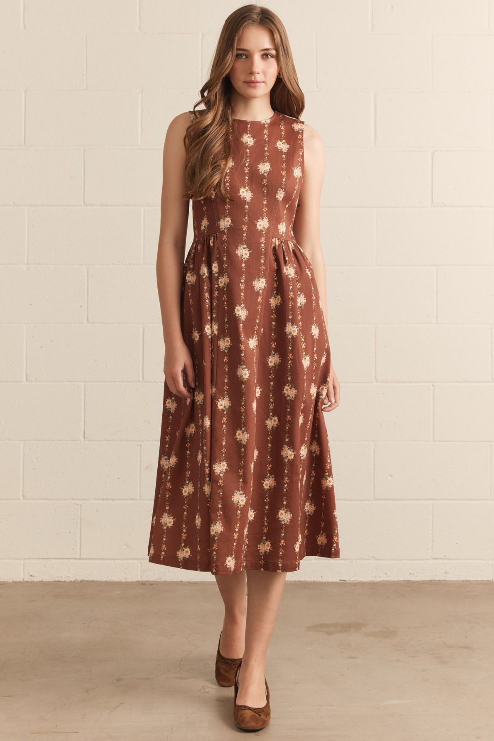 Woman wearing a brown floral dress against a white brick wall.