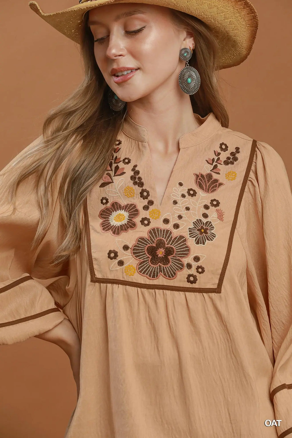 Woman wearing a beige embroidered blouse with a brown background