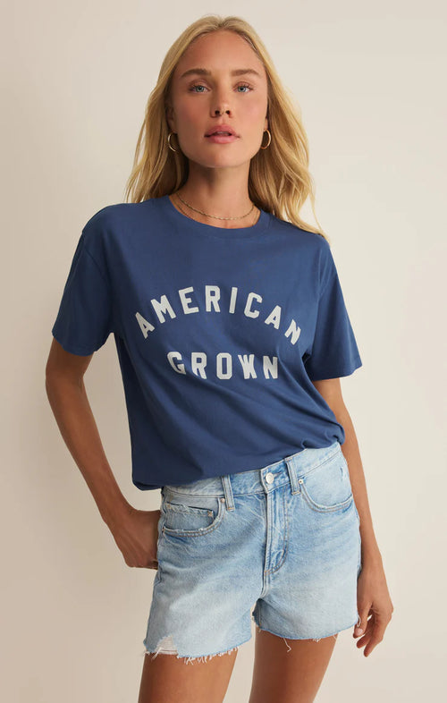 Woman wearing a blue 'American Grown' t-shirt and denim shorts on a beige background