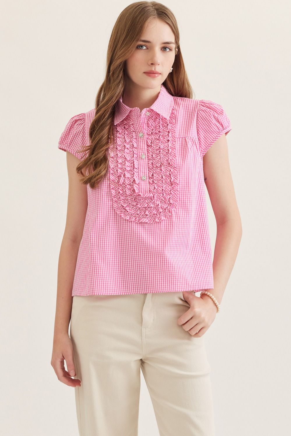 Woman wearing a pink checkered blouse with ruffled details on a beige background