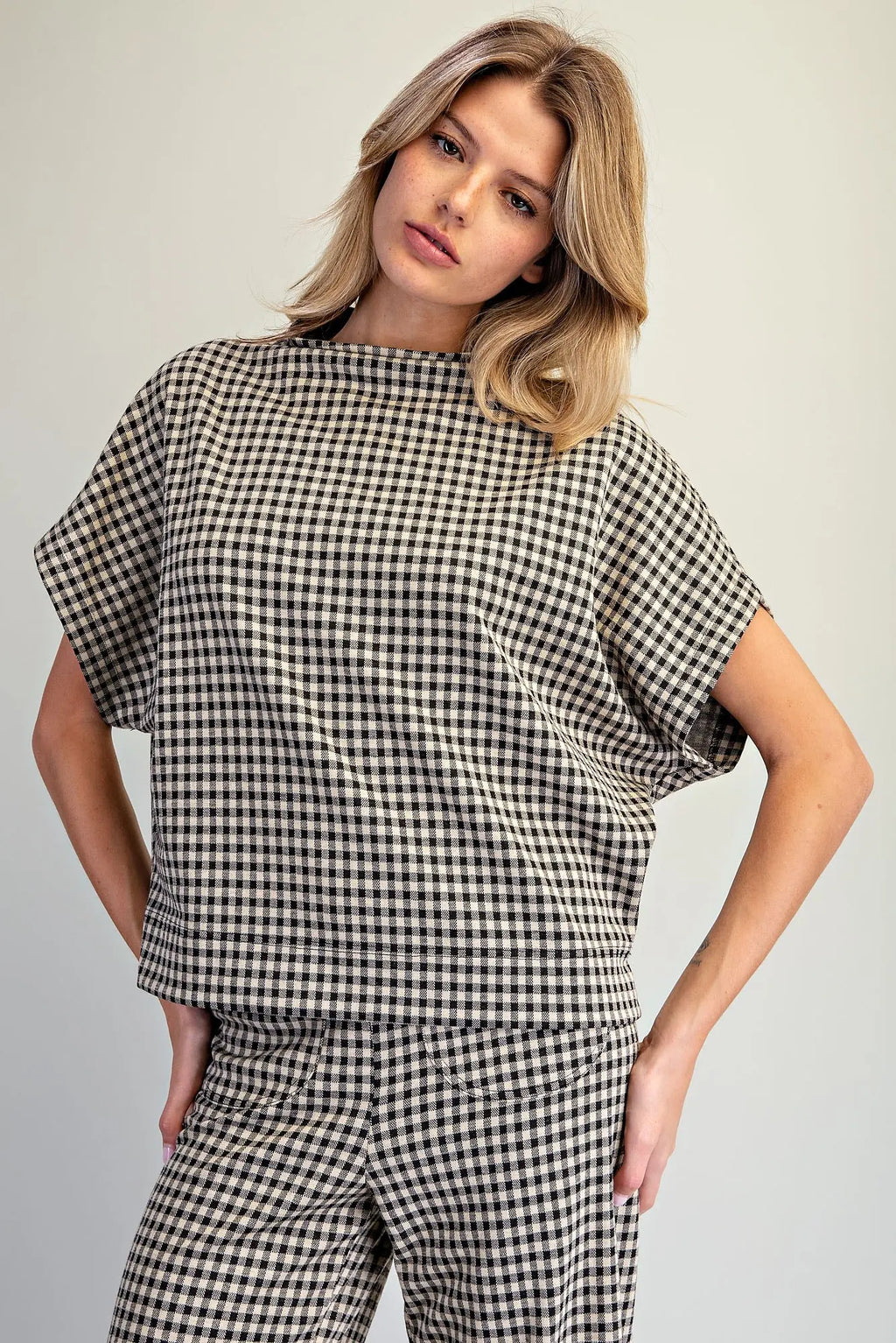 A woman modeling a matching black and white gingham check short-sleeve top and trousers set against a plain light gray studio background.