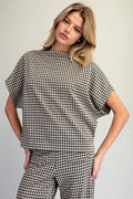 A woman modeling a matching black and white gingham check short-sleeve top and trousers set against a plain light gray studio background.