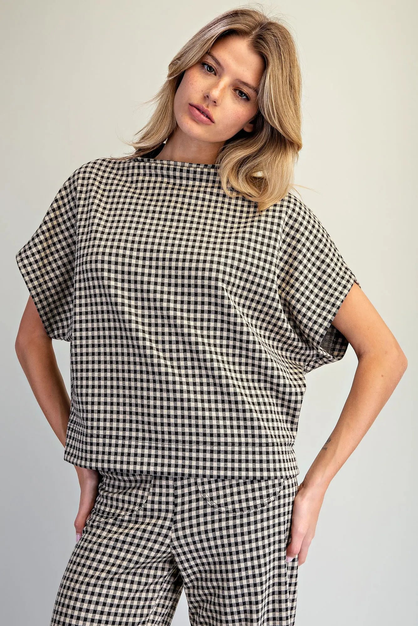 A woman modeling a matching black and white gingham check short-sleeve top and trousers set against a plain light gray studio background.
