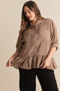 Woman wearing a brown and white checkered blouse with a ruffled bottom against a beige wall.