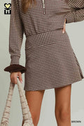 Person wearing a brown and white checkered dress with a plain background