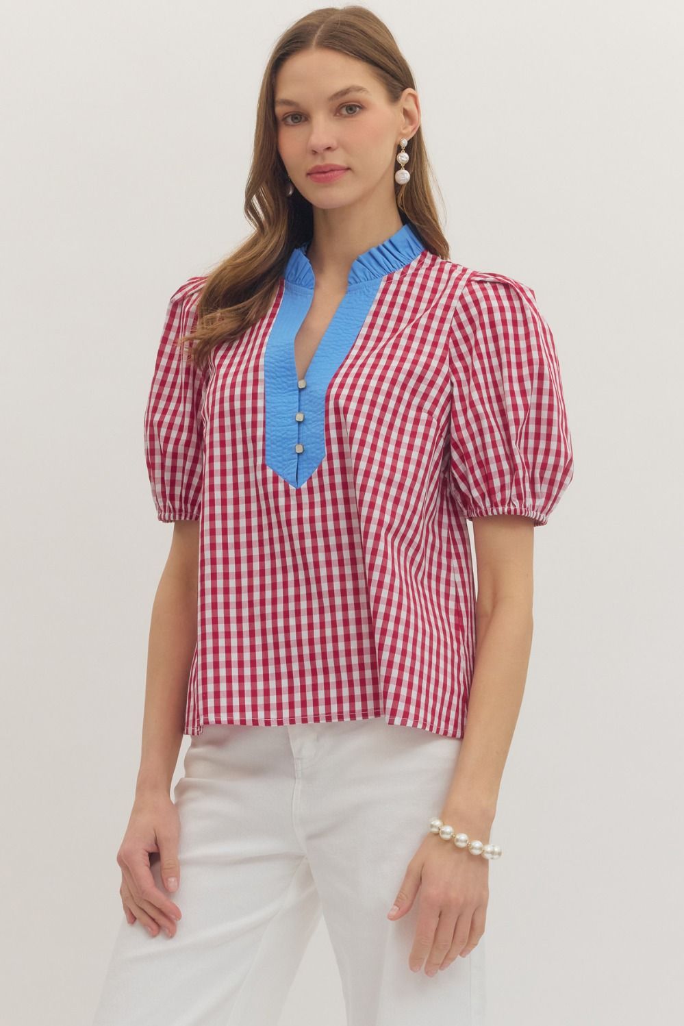 Woman wearing a red and white checkered blouse with blue neckline on a plain background