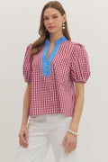 Woman wearing a red and white checkered blouse with blue neckline on a plain background