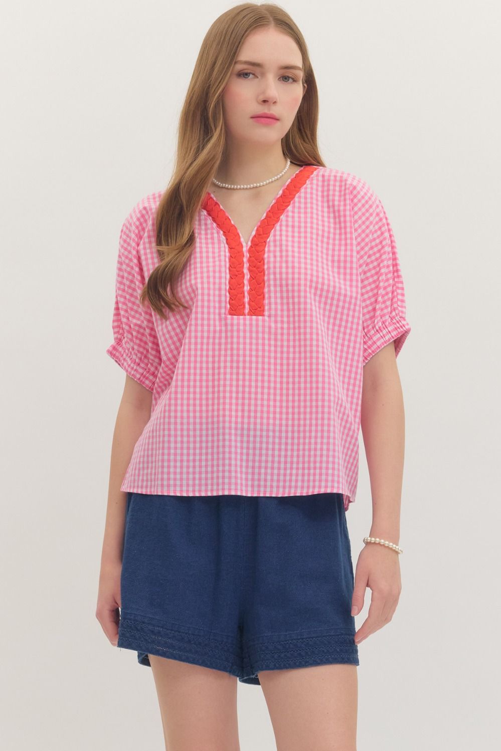 Woman wearing a pink checkered top with red trim and blue shorts on a white background