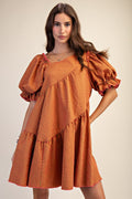 Woman wearing an orange checkered dress with puffed sleeves on a beige background