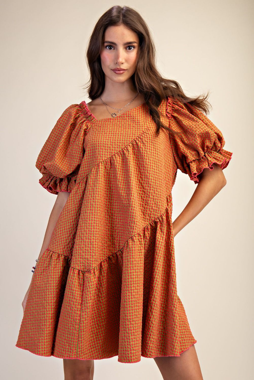 Woman wearing an orange checkered dress with puffed sleeves on a beige background