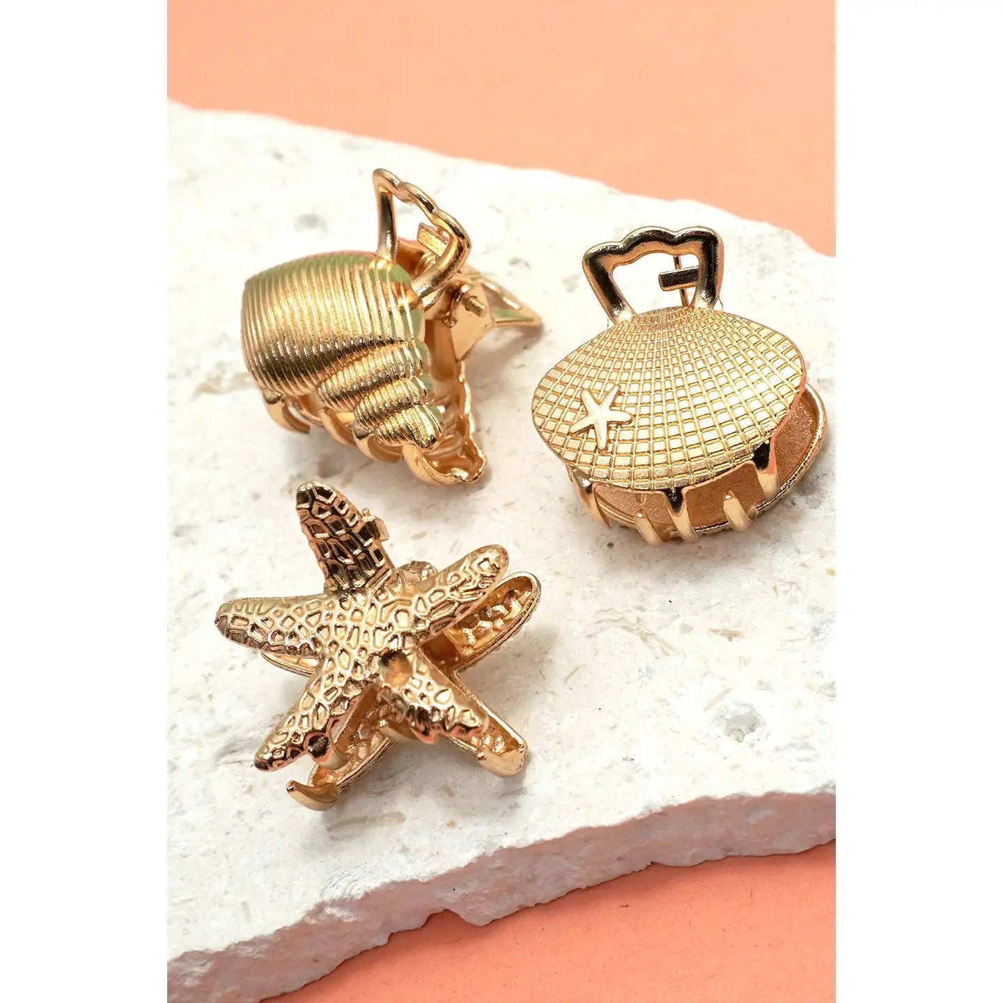 Gold sea-themed cufflinks including a shell, starfish, and airship on a textured surface.
