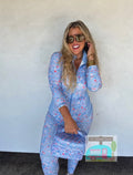 Woman wearing a blue floral outfit with sunglasses, standing against a white wall.