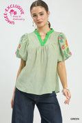 Woman wearing a green blouse with floral embroidery on a white background