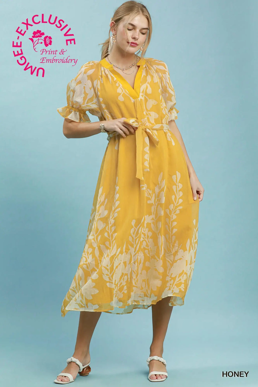 Woman wearing a yellow dress with floral pattern on a blue background, featuring Umgee Exclusive branding.