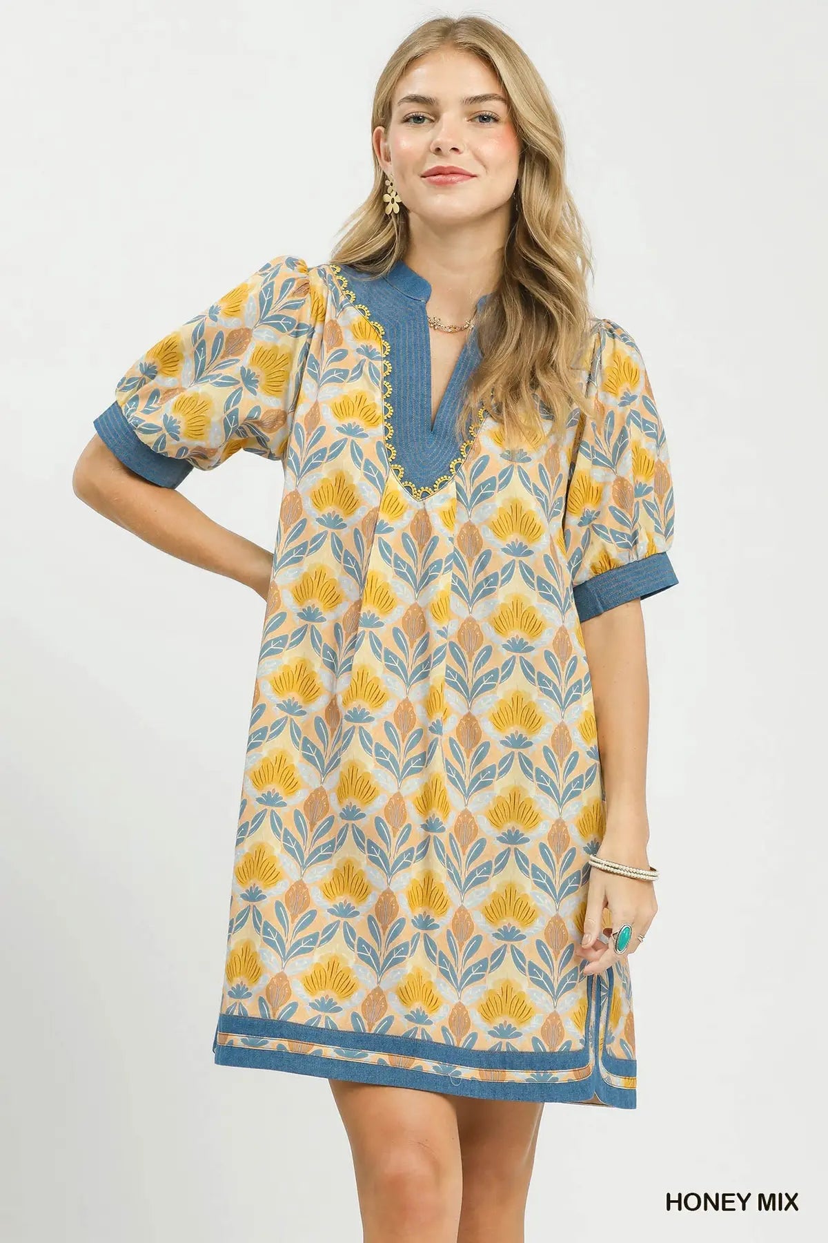Woman wearing a patterned dress with a honey mix color scheme on a white background