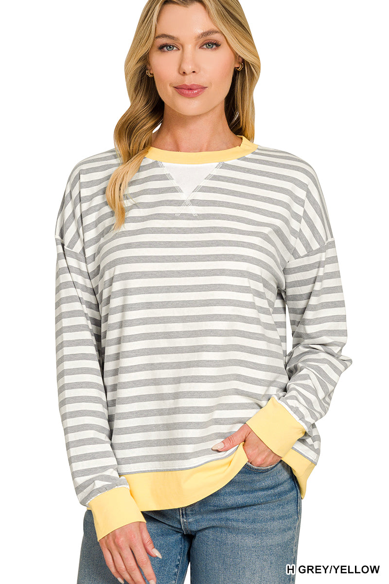 A woman wearing a grey and yellow striped long-sleeve top with solid yellow trim at the collar, cuffs, and hem, paired with blue jeans against a white background.