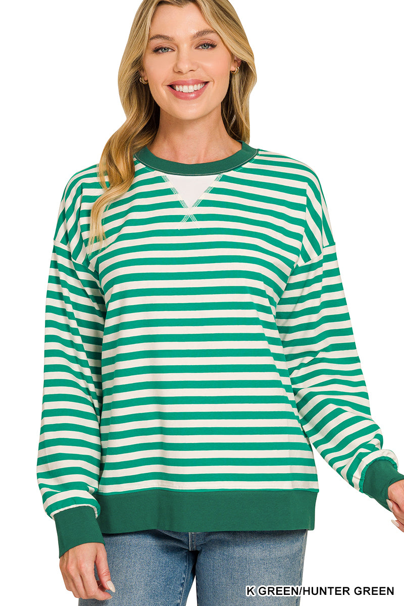A woman wearing a green and white horizontally striped long-sleeve crewneck sweater, paired with blue jeans, against a plain white background.
