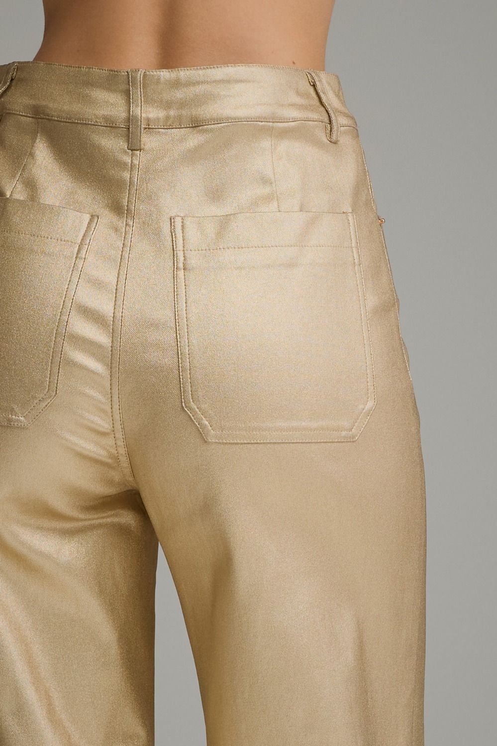Close-up back view of a person wearing shiny metallic gold pants, showing the waistband, belt loops, and back pocket details against a plain gray background.