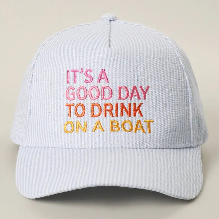 White cap with colorful text 'It's a good day to drink on a boat' on a beige background