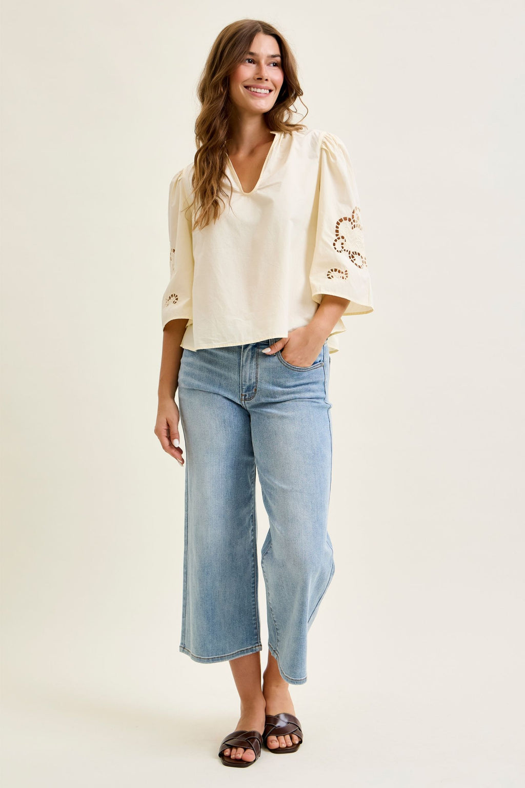Woman wearing a cream blouse with floral embroidery and light blue jeans on a white background