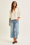 Woman wearing a cream blouse with floral embroidery and light blue jeans on a white background
