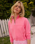 Woman wearing a pink quarter-zip sweatshirt outdoors with greenery in the background