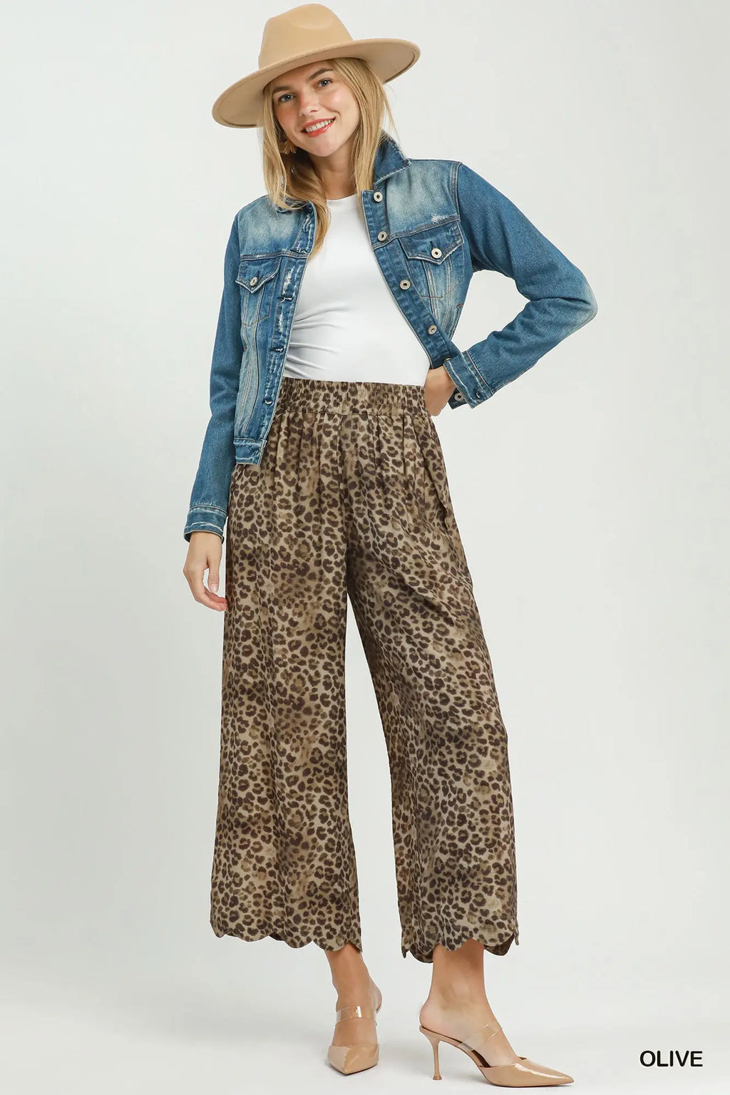 Woman wearing a denim jacket, white top, leopard print pants, and beige hat on a white background