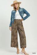 Woman wearing a denim jacket, white top, leopard print pants, and beige hat on a white background